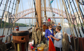 Nick and Evi work on the main mast flag with the Hellsgate Bridge looming in the background.