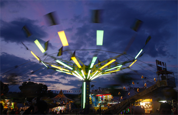 An animated sequence of the Swinger ride dominating an illuminated carnival at dusk.